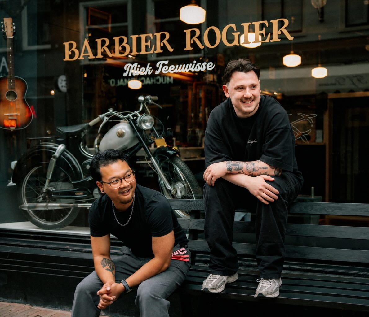 Mick en Kit, barbiers bij Barbier Rogier Haarlem, lachend op een bankje voor de winkel